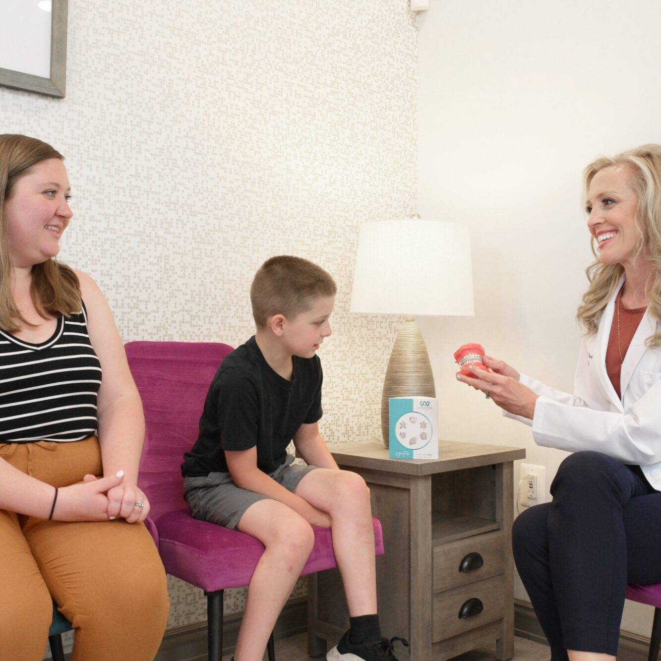 Child seated with parent in orthodontic office, Dr. Bowen explaining treatment using model, highlighting Bowen Family Orthodontics' welcoming environment for new patients.