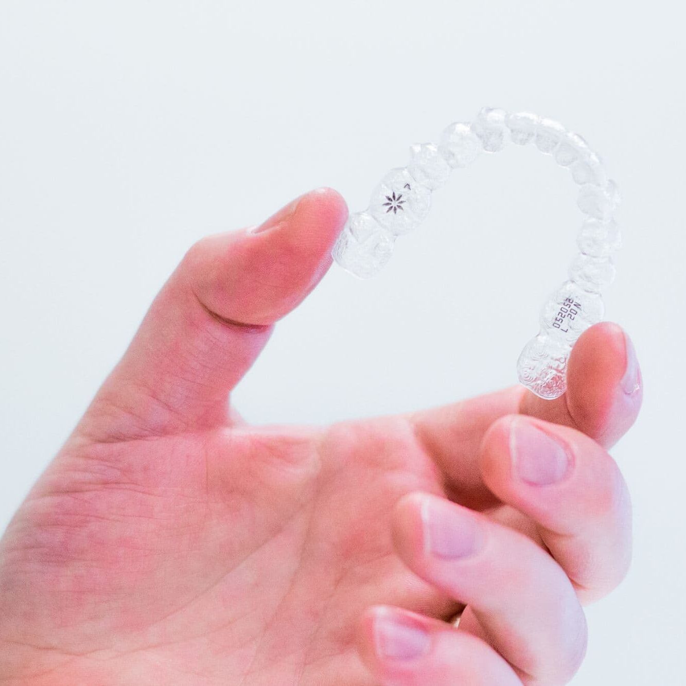 Hand holding clear Invisalign aligner, representing orthodontic treatment options at Bowen Family Orthodontics for Mullica Hill patients.
